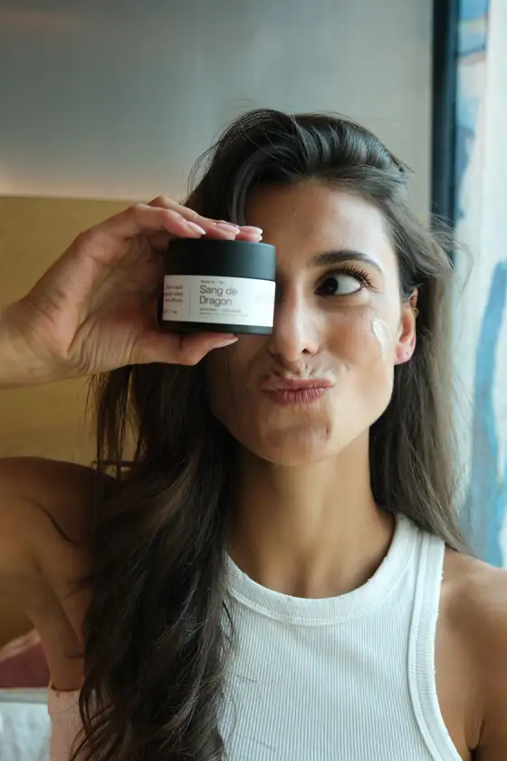 Femme tenant la Crème de Jour Sang de Dragon Skineance, une noisette de crème sur la joue